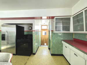 Kitchen with black / electric stove, tile walls, stainless steel fridge, a wainscoted wall, and white cabinetry