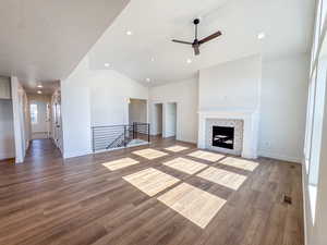 Unfurnished living room featuring ceiling fan, lofted ceiling, wood finished floors, a tiled fireplace, and recessed lighting