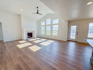 Unfurnished living room with a ceiling fan, wood finished floors, a fireplace, vaulted ceiling, and a textured ceiling