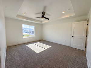 Empty room with a raised ceiling, ceiling fan, carpet floors, a smoke detector, and a textured ceiling
