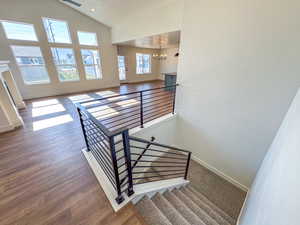 Stairs with a chandelier, wood finished floors, and high vaulted ceiling