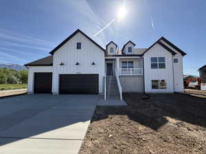 Modern farmhouse featuring board and batten siding, stairs, an attached garage, and driveway