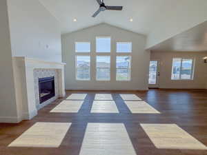 Unfurnished living room featuring ceiling fan, a tile fireplace, high vaulted ceiling, and dark wood-style flooring