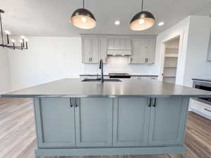 Kitchen featuring exhaust hood, gray cabinets, wood finished floors, a textured ceiling, and recessed lighting