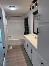 Bathroom with a textured ceiling, wood finished floors, shower / bath combo, and vanity