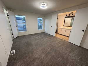 Unfurnished bedroom with light colored carpet, a textured ceiling, and ensuite bath