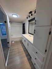Bathroom featuring a textured ceiling, vanity, shower / tub combo with curtain, wood finished floors, and track lighting