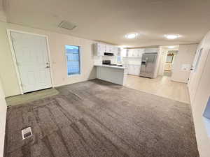 Kitchen featuring stainless steel appliances, a peninsula, lofted ceiling, under cabinet range hood, and white cabinetry