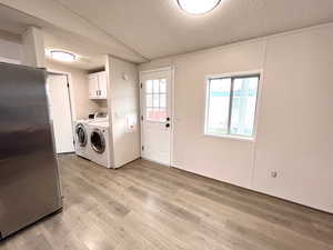 Clothes washing area featuring cabinet space, washer and clothes dryer, light wood-type flooring, and a textured ceiling