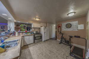 Kitchen featuring white appliances, a sink, white cabinetry, light countertops, and a textured ceiling