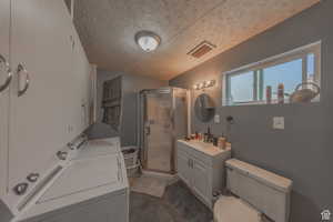 Full bath with washer and clothes dryer, a shower stall, a textured ceiling, toilet, and vanity