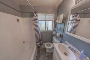 Full bath featuring toilet, shower / tub combo, tile patterned floors, vanity, and a textured ceiling