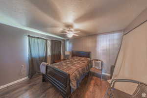 Bedroom with wood finished floors, baseboards, a textured ceiling, a ceiling fan, and wooden walls