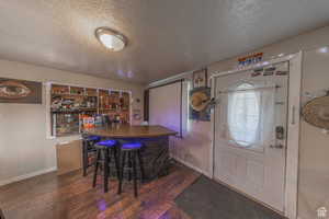 Indoor dry bar with a textured ceiling, wood finished floors, and baseboards