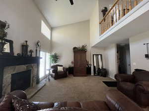 Living room featuring high vaulted ceiling, carpet floors, a stone fireplace, ceiling fan, and baseboards