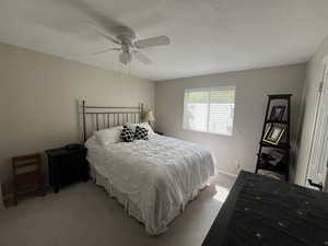 Bedroom featuring light colored carpet, ceiling fan, baseboards, and a textured ceiling
