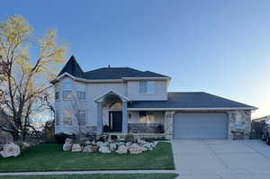 View of front of house featuring an attached garage, driveway, stone siding, and stucco siding