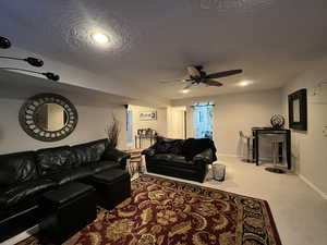 Carpeted living area with ceiling fan, baseboards, and a textured ceiling