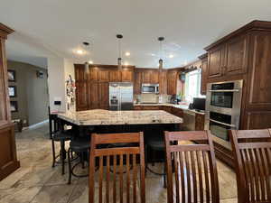 Kitchen with stainless steel appliances, a center island, a kitchen bar, hanging light fixtures, and baseboards