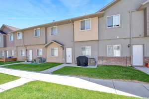 Rear view of property featuring brick siding, a lawn, central AC, and stucco siding