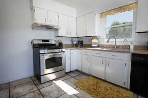 Kitchen with gas range, under cabinet range hood, a sink, and white cabinets