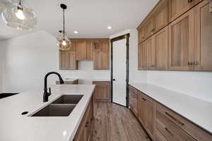 Kitchen with brown cabinets, light wood finished floors, pendant lighting, recessed lighting, and light stone countertops