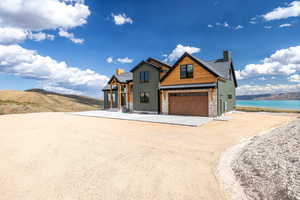 Modern inspired farmhouse with a chimney, dirt driveway, board and batten siding, stone siding, and a water view