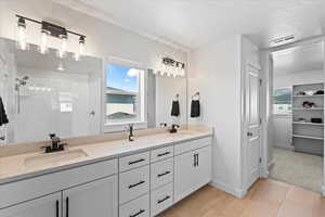 Primary bathroom suite with tile patterned floors, healthy amount of natural light, double vanity, and a tile shower