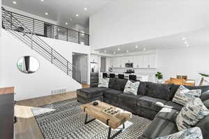 Living room featuring light wood-style floors, recessed lighting, stairs, a towering ceiling