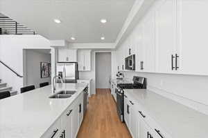 Kitchen with stainless steel appliances, a sink, recessed lighting, light wood-style floors, and white cabinetry