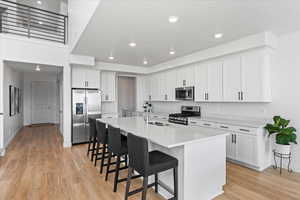 Kitchen featuring stainless steel appliances, a sink, light wood-style flooring, a kitchen breakfast bar, and white cabinets