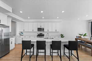 Kitchen with stainless steel appliances, a sink, light countertops, a breakfast bar, and recessed lighting