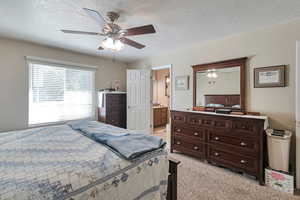 Bedroom featuring a textured ceiling, light carpet, a ceiling fan, and ensuite bath