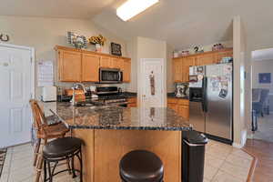 Kitchen with appliances with stainless steel finishes, vaulted ceiling, a sink, a peninsula, and a kitchen bar