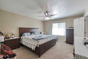 Bedroom featuring a textured ceiling, light colored carpet, baseboards, and ceiling fan
