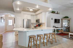 Kitchen with appliances with stainless steel finishes, ceiling fan, arched walkways, a peninsula, and a sink