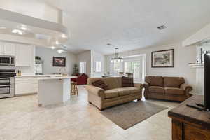 Living area with a ceiling fan, a chandelier, light tile patterned floors, and a textured ceiling