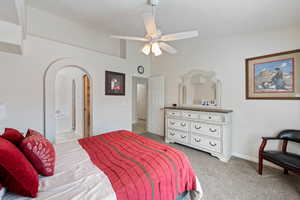 Bedroom with arched walkways, baseboards, carpet flooring, a ceiling fan, and connected bathroom