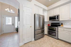 Kitchen featuring appliances with stainless steel finishes, a chandelier, light tile patterned flooring, lofted ceiling, and light countertops
