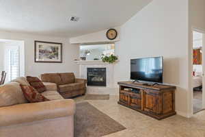 Living area featuring a high end fireplace, light tile patterned flooring, a textured ceiling, and vaulted ceiling