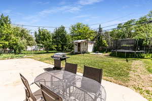 View of patio featuring a trampoline, a grill, outdoor dining area, a storage unit, and an outbuilding