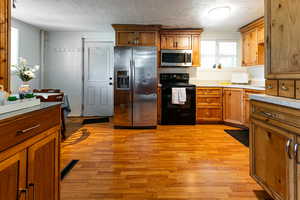 Kitchen with stainless steel appliances, light wood-style floors, a textured ceiling, brown cabinetry, and light countertops