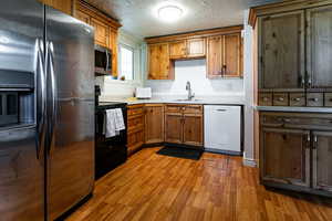 Kitchen featuring stainless steel appliances, a sink, wood finished floors, brown cabinets, and light countertops