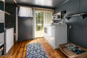 Laundry room with wood-type flooring, washing machine and clothes dryer, and wooden walls