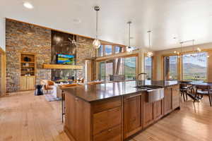 Kitchen featuring a sink, dark countertops, a stone fireplace, light wood finished floors, and a kitchen island with sink