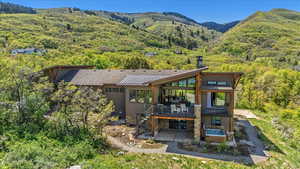 Back of property featuring a patio area, a standing seam roof, stone siding, a forest view, and a deck with mountain view