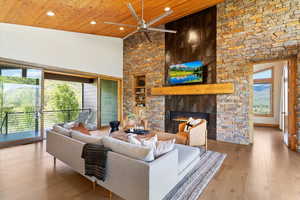 Living area featuring a ceiling fan, built in shelves, a stone fireplace, wood ceiling, and recessed lighting