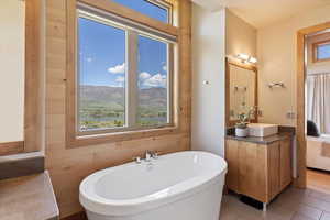Ensuite bathroom featuring healthy amount of natural light, a soaking tub, vanity, and tile patterned floors
