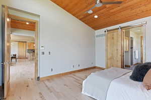 Bedroom with a barn door, light wood-type flooring, lofted ceiling, recessed lighting, and baseboards