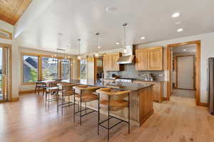 Kitchen featuring wall chimney exhaust hood, light wood-style flooring, a spacious island, tasteful backsplash, and recessed lighting